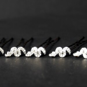 May include: Six silver hair clips with a wavy design adorned with clear rhinestones.