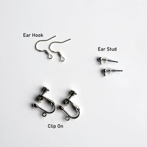 May include: Three different types of earring findings: ear hooks, ear studs, and clip-on earrings. All findings are silver in color.