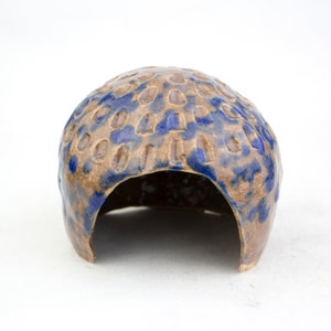 May include: A brown and blue ceramic reptile hide with a textured surface. The hide has a large opening for the reptile to enter.