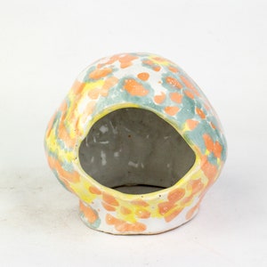 May include: A ceramic planter with a unique, abstract design featuring yellow, orange, and green paint splatters. The planter has a large opening on the side, making it ideal for displaying small plants or succulents.