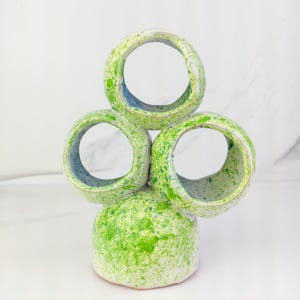 May include: A ceramic sculpture with a green and white speckled glaze. The sculpture is made up of three stacked rings with a round base.