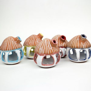 May include: Five small ceramic houses with white and brown paint, each with a different colored interior. The houses are arranged in a semi-circle on a white surface.