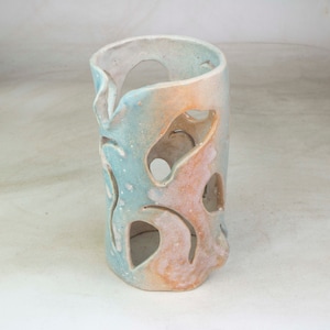 May include: A ceramic vase with a light blue and peach glaze. The vase has a cylindrical shape with cut-out designs.