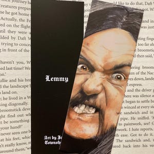 May include: A black bookmark featuring a detailed portrait of Lemmy Kilmister with a stern expression. The bookmark has the name "Lemmy" in white text and "Art by Jo Townshend" at the bottom.