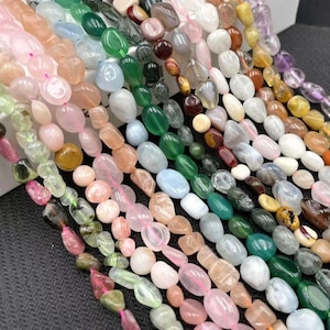 May include: Multiple strands of polished, tumbled gemstone beads in a variety of colours including pink, green, blue, white, brown, and purple. The beads are oval and irregular in shape, strung on thin threads, creating a vibrant, multi-coloured display.