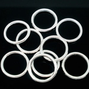 May include: A group of silver jump rings, a type of jewellery finding, arranged on a black background.