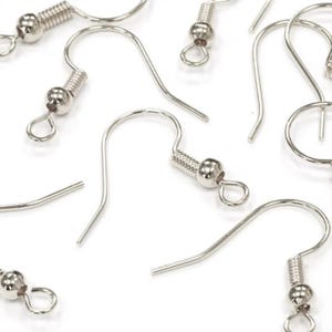 May include: Close-up of several silver-colored earring hooks, scattered against a white background. Each hook features a coiled spring detail and a small, round bead. The hooks are designed for jewelry making and crafting.