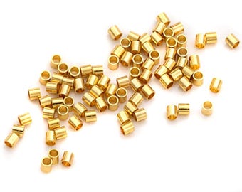May include: A collection of small, cylindrical gold-colored metal beads scattered on a white surface. Each bead has a hole running through the center, and they appear to be made of a shiny, metallic material. These beads are likely used for jewelry making or other craft projects.