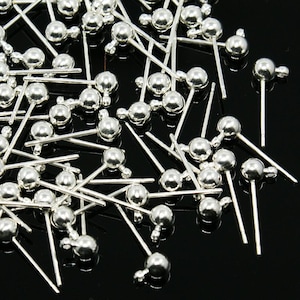 May include: A collection of silver-toned metal earring posts featuring a small spherical ball at the top and a tiny integrated loop for attaching charms or dangles. These jewellery findings have a smooth, reflective finish and straight pins.