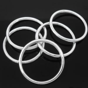 May include: A set of five silver-toned metal rings, stacked and overlapping. The rings are smooth and round, with a polished finish.