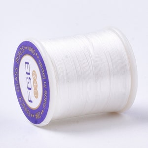 May include: A white spool of thread labelled "Fancy Glass Beads #02 FCG Made in Japan 50m"