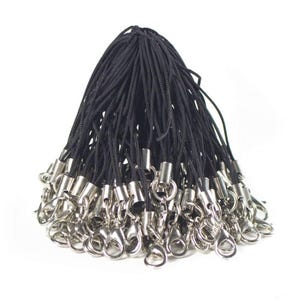 May include: A collection of black lanyards, each with a silver-coloured metal lobster claw clasp and barrel connector. The lanyards are made from a thin, woven cord. The clasps are shiny. The lanyards are grouped together against a white backdrop.