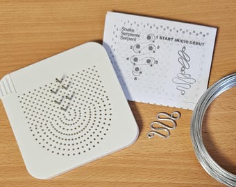 May include: A white beading board with a spiral pattern and directional arrows, a silver wire snake-shaped bead, a diagram with the text "Snake Serpentine Serpent" and a coil of silver wire. Craft supplies.