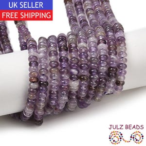 May include: A close-up of multiple strands of purple gemstone beads. The beads are a mix of lavender and violet hues, with a rounded shape. The image includes the text "JULZ BEADS".