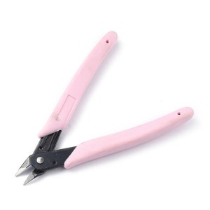 May include: Wire cutters with pink handles and black cutting blades. The handles are a soft pink and have a smooth, rounded shape. The cutting blades are made of a dark metal and have sharp edges.
