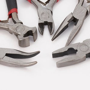 May include: A selection of metal hand tools, including pliers and a hammer-style tool, are displayed against a white backdrop. The tools feature black and red handles. The pliers have diverse head shapes for various tasks.
