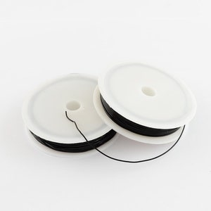 May include: Two spools of black wire wound around white plastic bobbins. The wire is thin and appears to be for jewellery making.