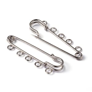 May include: Two silver safety pins with multiple loops on each pin. The pins are open and ready to be used.