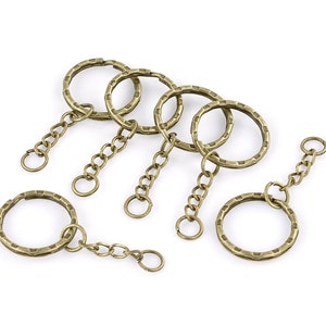 May include: Six antique gold keyrings with textured rings and attached chains. The keyrings are arranged on a white background.