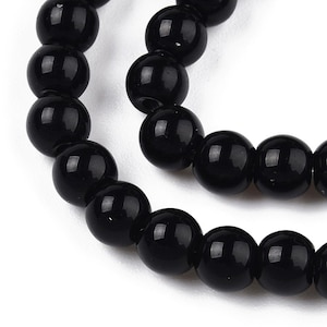 May include: Close-up of a strand of black, glossy, round beads. The beads are uniform in size and appear to be made of a smooth, polished material. The beads are strung together, suggesting a necklace or bracelet.