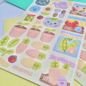 K&ouml;nnte beinhalten: Ein Bogen mit bunten Aufklebern zum Thema Gartenarbeit. Designs umfassen Topfpflanzen, Karotten, Saatgutt&uuml;ten mit der Aufschrift "tomato", "sugarsnap" und "carrot" sowie ein niedliches Hasengesicht. Das Wort "ORGANIC" ist ebenfalls enthalten.