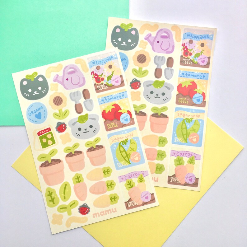 K&ouml;nnte beinhalten: Zwei Stickerb&ouml;gen mit Illustrationen zum Thema Garten. Designs umfassen ein Katzen-Gesicht, eine Gie&szlig;kanne, eine Sonnenblume, Tomaten, Karotten und Sament&uuml;ten. Die Aufkleber tragen die W&ouml;rter "ORGANIC" und "mamu".
