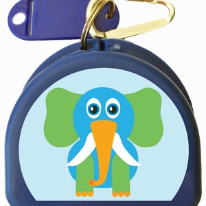 May include: A navy blue dental floss container with a cartoon elephant design. The elephant is blue with green ears and legs, an orange trunk, and white tusks. Includes a blue plastic key tag and a gold carabiner clip.