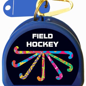 May include: A blue plastic container with a gold carabiner clip. The container has a black background with the words "FIELD HOCKEY" in white text and a design of colorful hockey sticks.