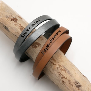 May include: Two leather bracelets with engraved messages. One bracelet is brown and says "Papa d'amour". The other bracelet is grey and says "Super papa".