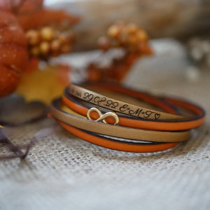 Op de afbeelding: Een meerlaags leren armband met een oneindigheidssymbool bedel. De armband is gegraveerd met de datum "29.08.22" en de tekst "E+M=T" met een hartje.