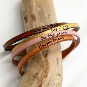 Peut inclure: Trois bracelets en cuir avec des messages gravés différents : "Follow your Dreams", "Be the storm" et "Carpe Diem". Les bracelets sont marron, or et rose.