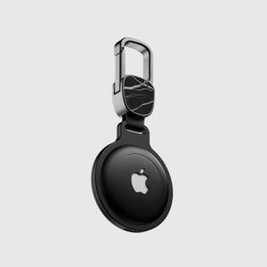 Könnte beinhalten: Ein schwarzer und silberner Schlüsselanhänger mit einem Marmormuster auf der Oberseite und einem Apple-Logo auf der Unterseite.