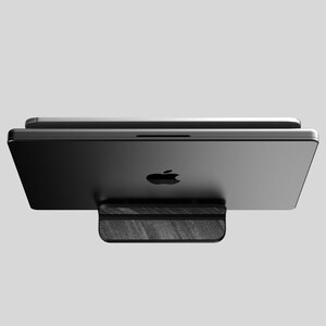 May include: A black laptop computer is sitting on a black wooden stand. The laptop is closed and the Apple logo is visible on the top of the lid.