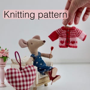 May include: A miniature red and pink knitted sweater with heart details is held up by a hand. A mouse doll sits in a miniature chair next to a red and white checkered heart ornament. The text "Knitting pattern" is displayed.