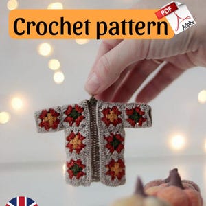 May include: A miniature crochet jacket with red, yellow, and green floral patterns is held by a hand. The text "Crochet pattern" is displayed in an orange box. Two small decorative pumpkins are in the background.