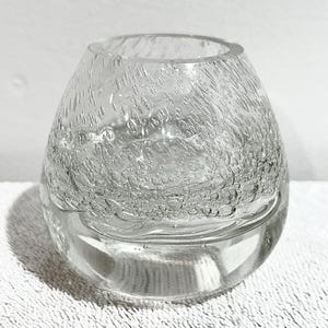 May include: Clear glass vase with a textured, bubble-like design. The vase has a rounded shape and a wide opening. The glass appears to be thick and sturdy. The vase is sitting on a white surface.