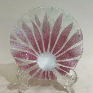 May include: A clear glass bowl with a scalloped edge and a radial pattern of speckled pink petals radiating from a solid white center. The bowl is supported by a transparent plastic stand, showcasing the translucent glass and textured pink design.