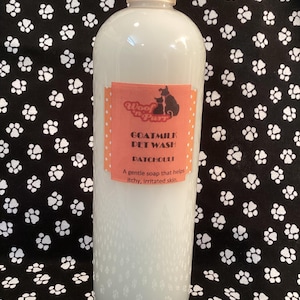 May include: A white plastic bottle of goat milk pet wash with a pink label that says "Woof 'n' Purr Goatmilk Pet Wash! Patchouli" and "A gentle soap that helps itchy, irritated skin."
