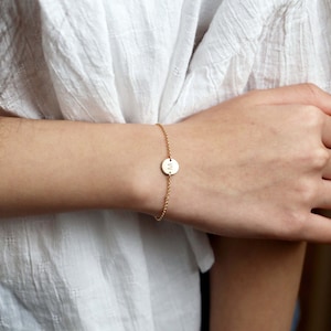 May include: A gold chain bracelet with a small round charm featuring the letter "M" engraved on it.