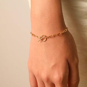 May include: A gold chain bracelet with a toggle clasp. The bracelet is made of a thick, chunky chain.