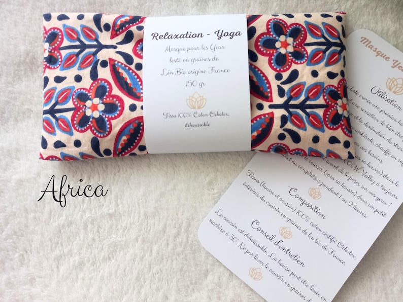 May include: A rectangular eye pillow with a cream background and a repeating floral pattern in navy blue, red, and light blue. A white paper band wraps around the center with the text Relaxation - Yoga, 150 gr, and Tissu 100% Coton Oeko-tex.