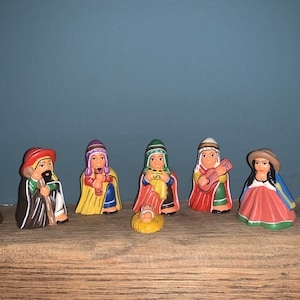 Pode incluir: Um presépio com um bebê Jesus de cerâmica, Maria, José e três reis magos. As figuras estão vestidas com roupas tradicionais coloridas e são cercadas por uma lhama e uma alpaca.