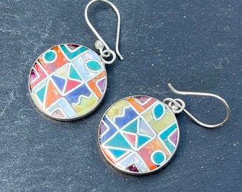 May include: A pair of silver earrings with round, colorful, geometric designs. The earrings are made of silver and feature a variety of colorful stones and materials.