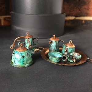 May include: A miniature tea set with a green and copper finish. The set includes a teapot, creamer, sugar bowl, and two teacups. The set is displayed on a copper tray.