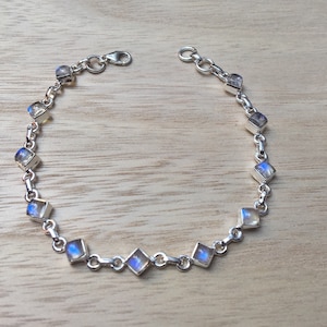 Puede incluir: Un brazalete de cadena de plata con gemas de piedra lunar de forma cuadrada. El brazalete tiene un cierre de langosta.