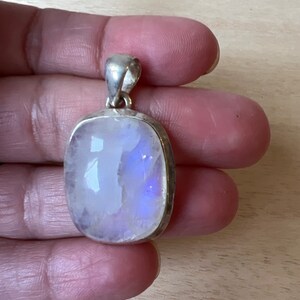 May include: A silver pendant with a large, oval-shaped moonstone. The moonstone is iridescent, with shades of blue and white.