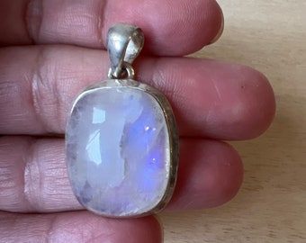 May include: A silver pendant with a large, oval-shaped moonstone. The moonstone is iridescent, with shades of blue and white.