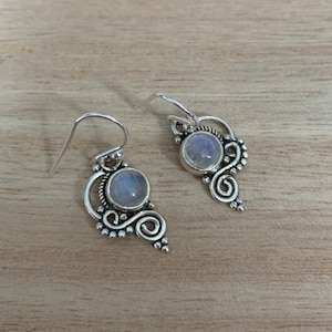 May include: A pair of silver earrings featuring a moonstone gemstone in each. The earrings have a delicate, ornate design.