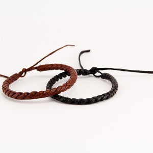 Peut inclure: Deux bracelets en cuir tressés, l'un brun et l'autre noir.