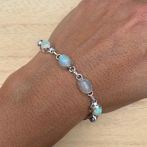 Peut inclure: Un bracelet en argent avec cinq pierres d'opale de forme ovale. Le bracelet est porté au poignet.